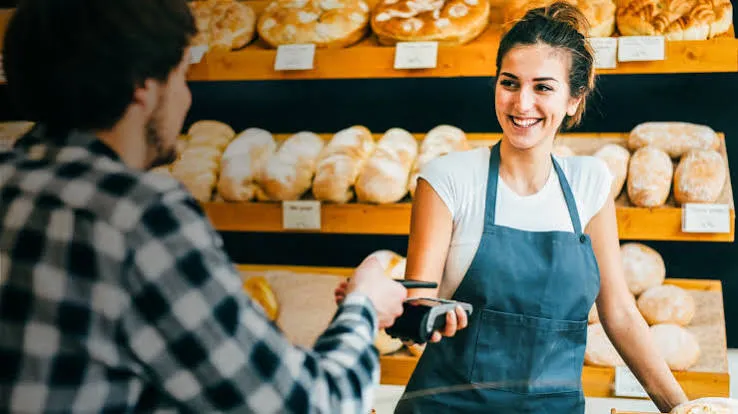 Una empleada con delantal cobra con un posnet a un cliente en una panadería.