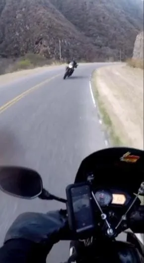 Una persona anda en moto por una ruta entre cerros y otra moto viene más adelante.