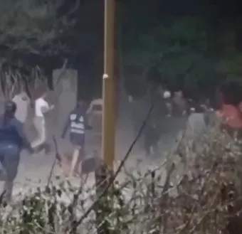 Un grupo de personas corre por una calle de tierra en medio de una nube de polvo junto a un poste de luz.