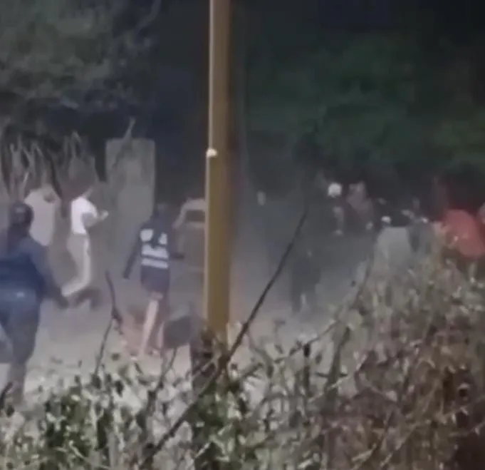 Un grupo de personas corriendo y cruzando una calle de tierra entre arbustos y postes.