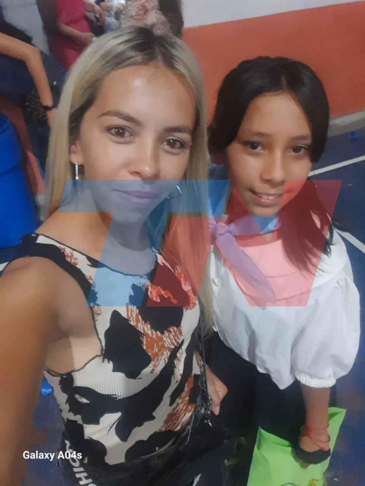Una mujer rubia y una nena con pañuelo lila al cuello se sacan una selfie en un interior.