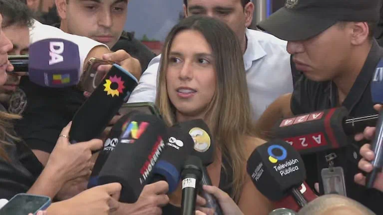 Una mujer habla rodeada de micrófonos de distintos canales y cronistas.