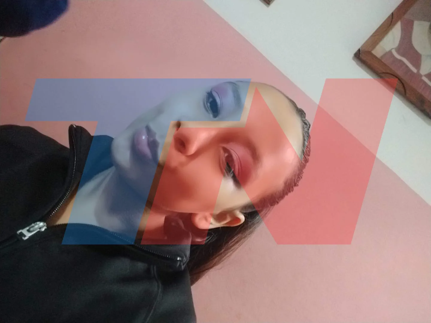 Una joven con campera negra y maquillaje en los ojos se saca una selfie en plano contrapicado.