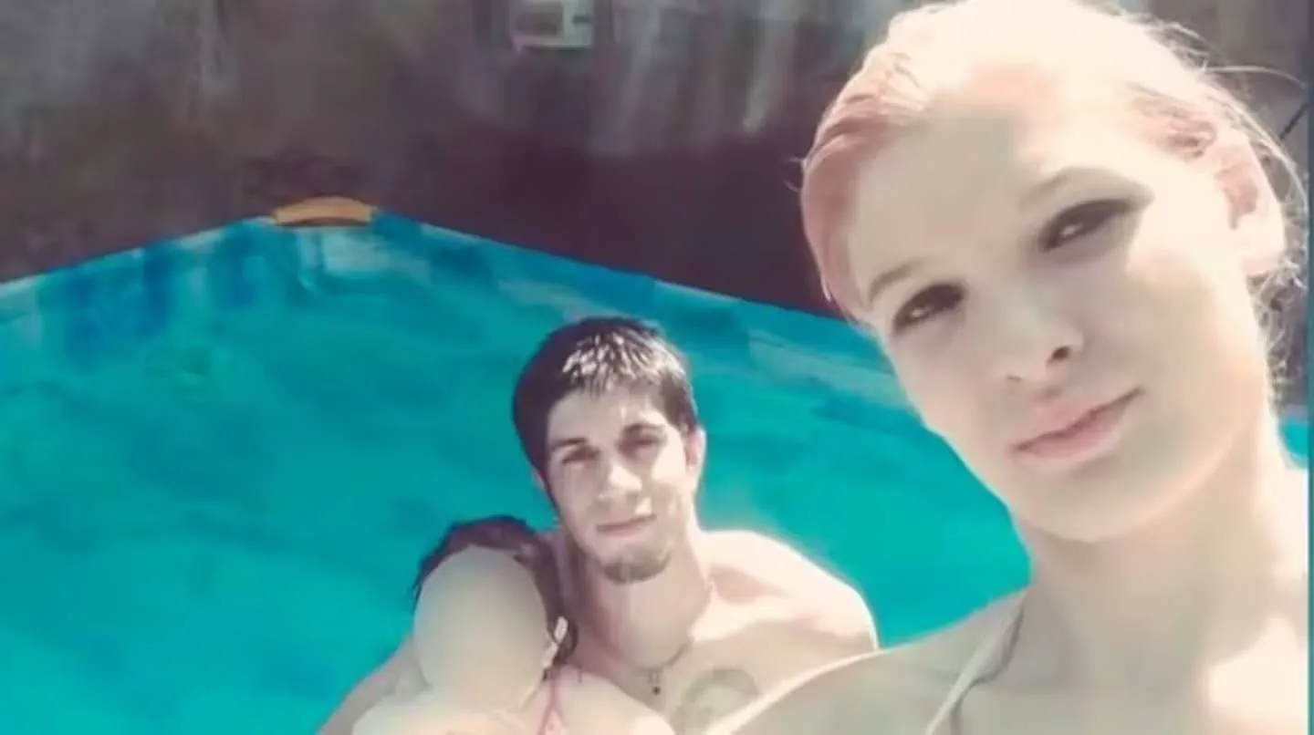 Una chica sonríe junto a un joven y un nene con la cara tapada en el agua de una pileta.