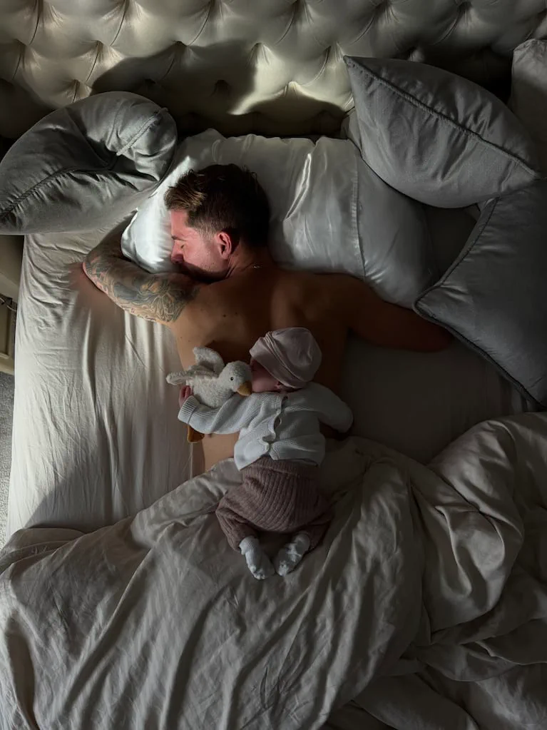 Un hombre duerme boca abajo en la cama con un bebé acostado sobre su espalda.