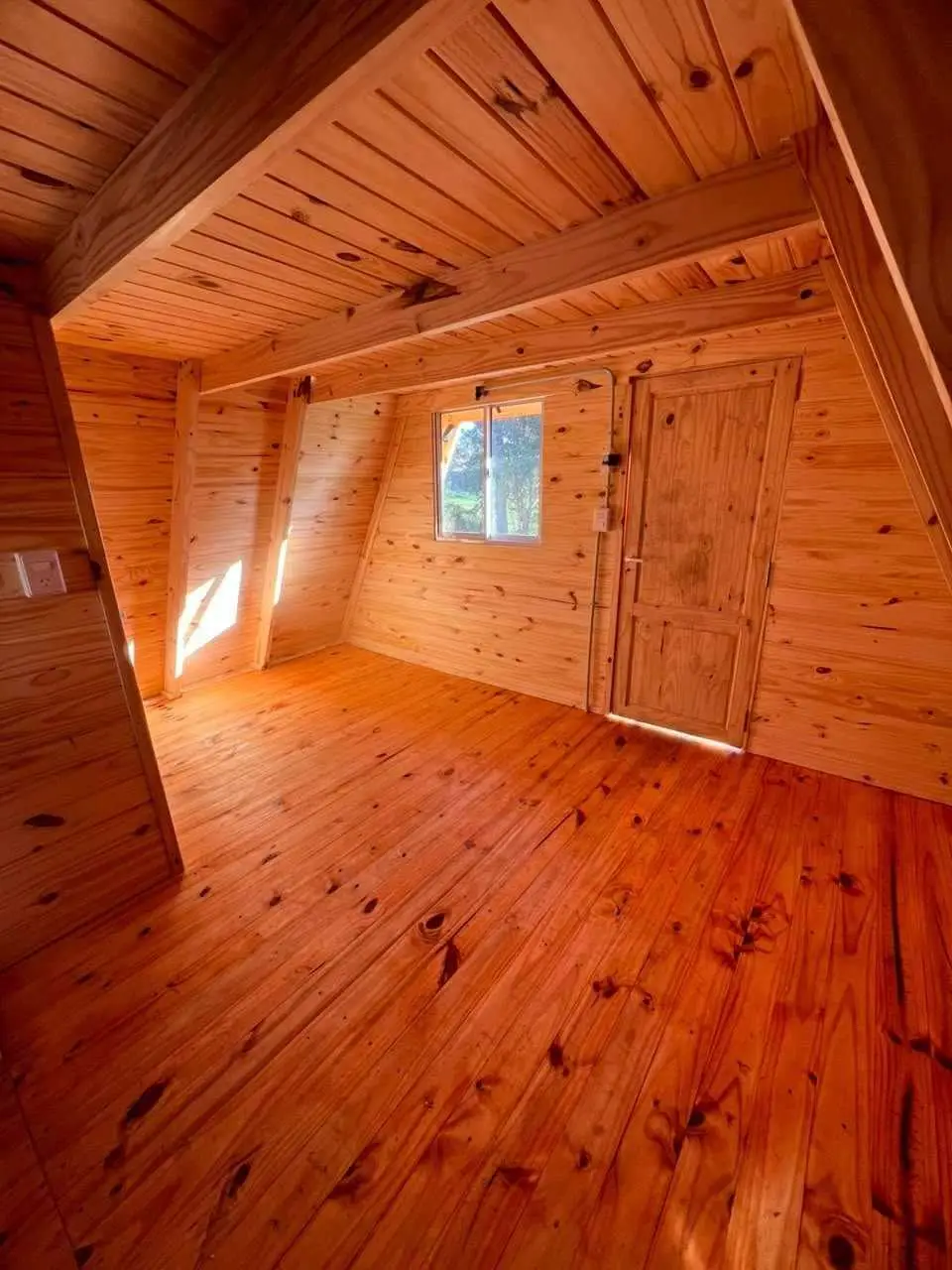 Ambiente vacío de madera con piso entablonado, una ventana al fondo y una puerta lateral.