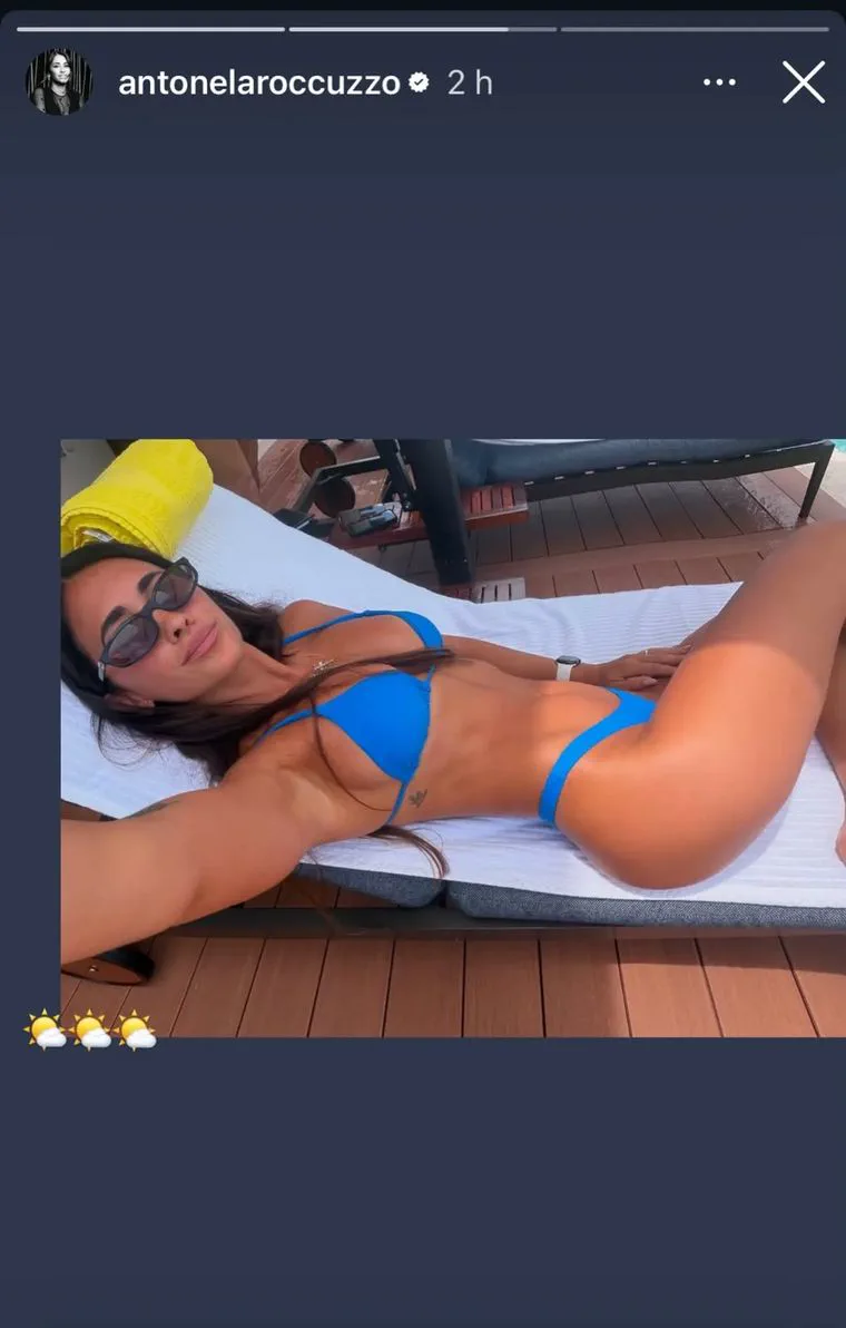 Antonela Roccuzzo toma una selfie acostada en una reposera al sol luciendo una bikini azul.