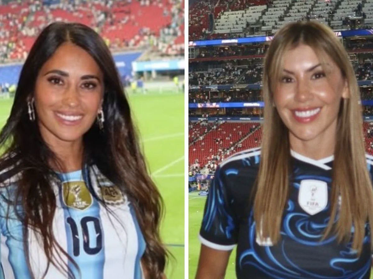 Antonela Roccuzzo y otra mujer sonríen con camisetas de la selección argentina en una cancha.