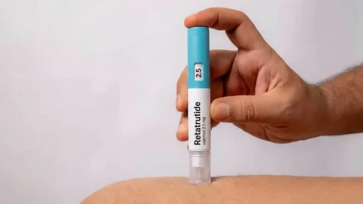 Una mano sostiene una lapicera inyectable de Retatrutide apoyada sobre la piel de un brazo o pierna.