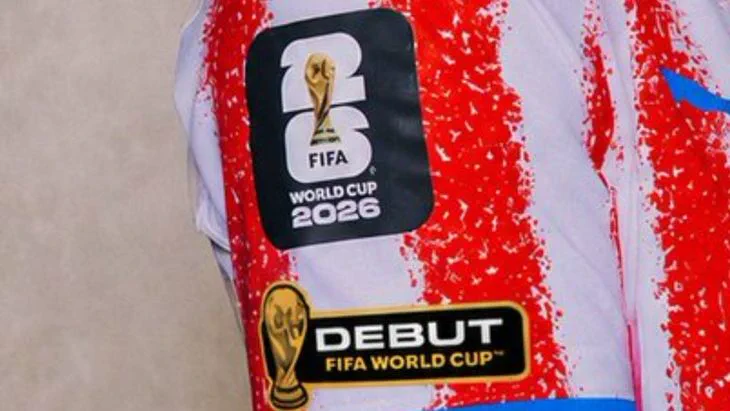 Detalle de una manga de camiseta blanca y roja con parches oficiales de la Copa del Mundo de la FIFA 2026.