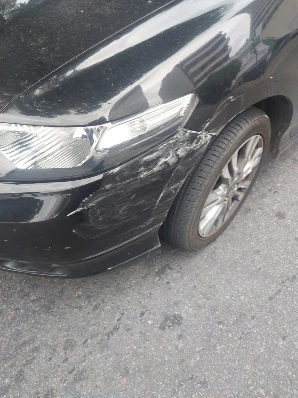 El paragolpes delantero y la óptica de un auto negro rayados y raspados tras un choque.