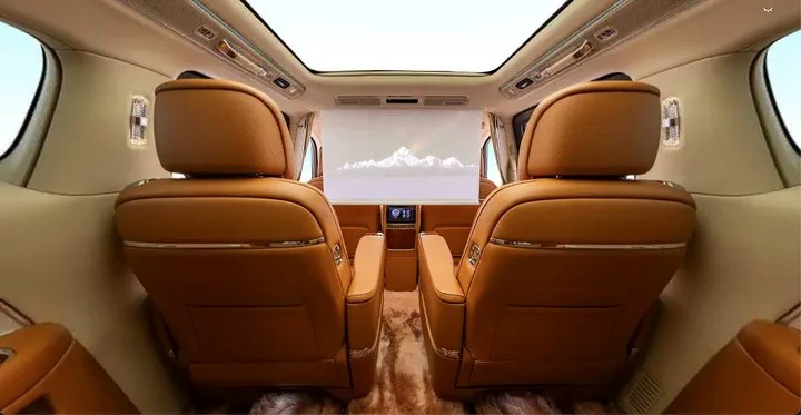 Asientos traseros tapizados en cuero marron y una pantalla colgante en el interior de un vehiculo de lujo.
