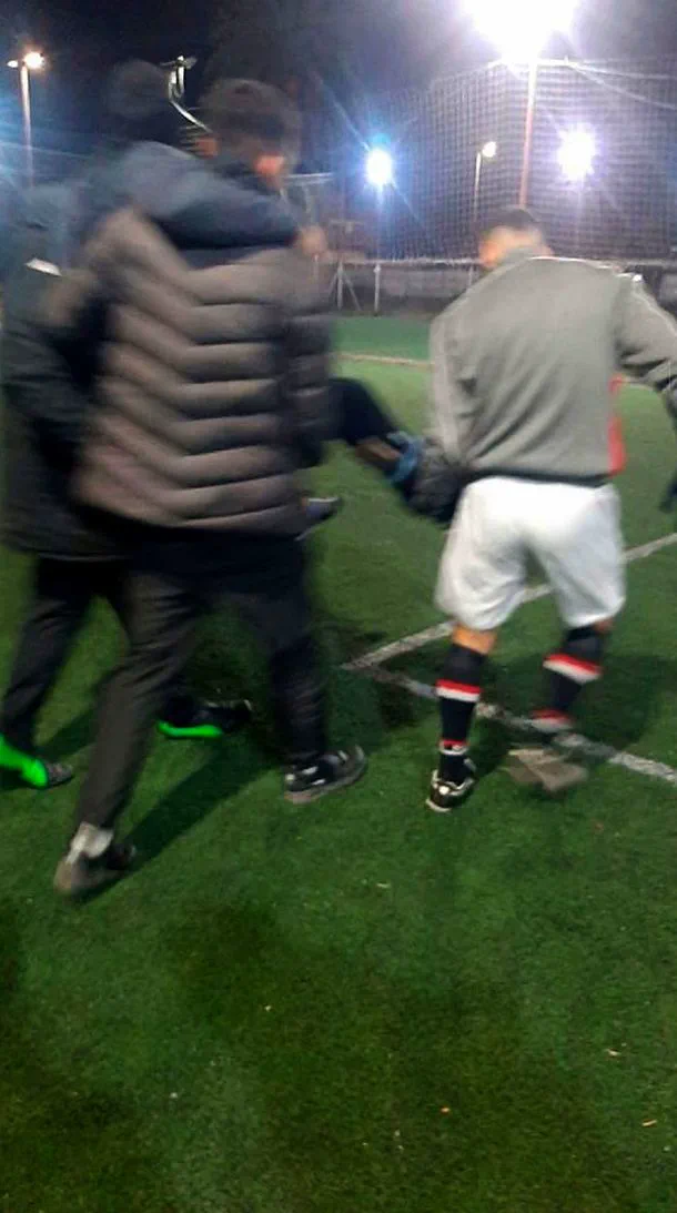 Tres personas asisten a otra persona caminando de noche sobre el cesped de una cancha deportiva.