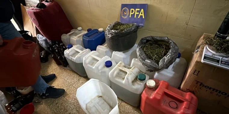 Varios bidones plasticos, bolsas con sustancia vegetal y un cartel de la Policia Federal Argentina en el piso.