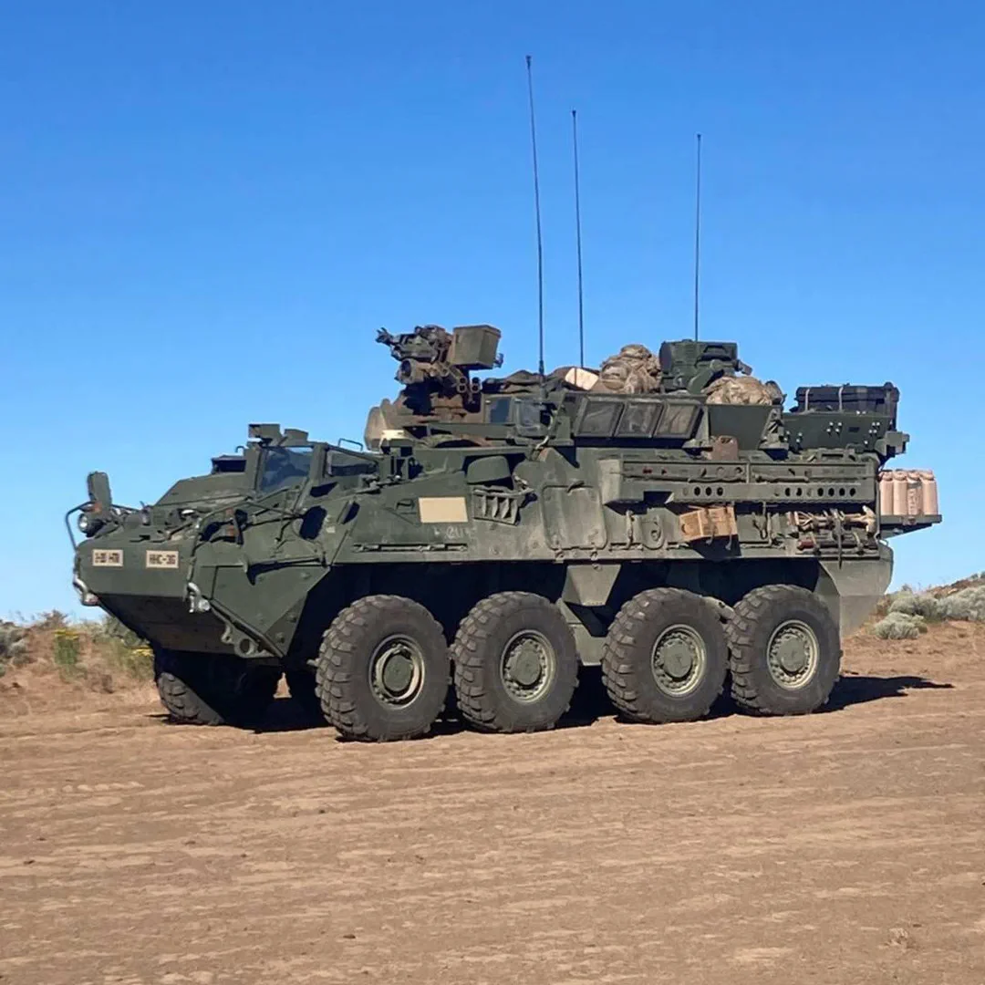 Un vehículo blindado militar de ocho ruedas se encuentra estacionado sobre un terreno árido bajo un cielo despejado.