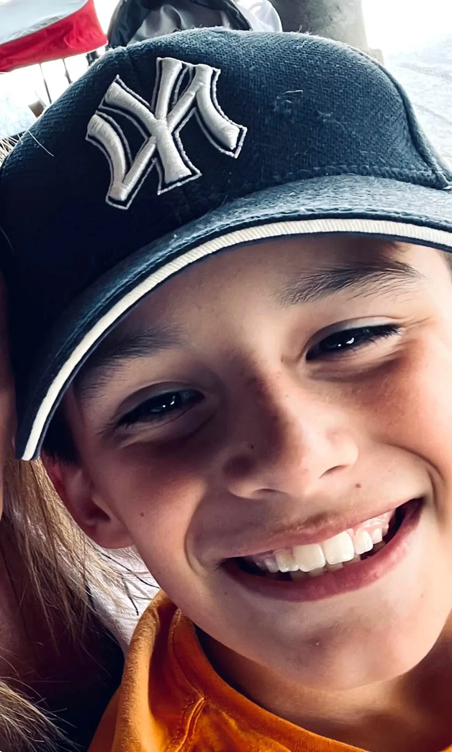 Un nene sonríe en primer plano llevando puesta una gorra oscura con visera de los New York Yankees.