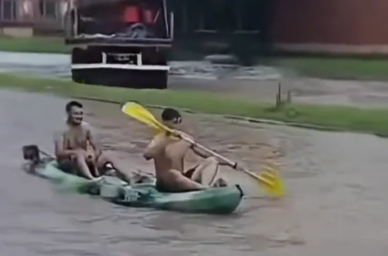 Dos jóvenes remando en un kayak por una calle completamente inundada.