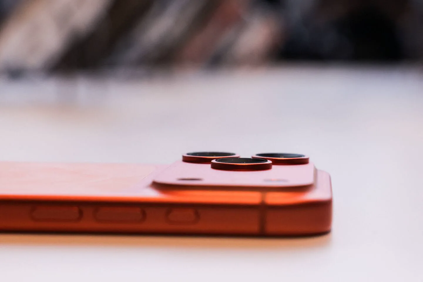 Primer plano del modulo de camaras y el borde lateral de un telefono celular de color naranja apoyado sobre una superficie.