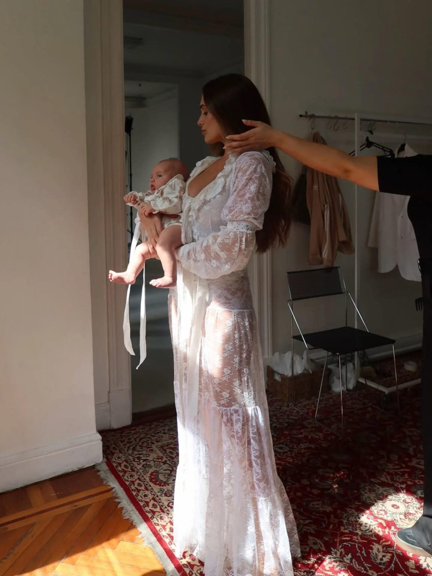 Camila Homs con vestido largo de encaje blanco sosteniendo a un bebé en brazos.