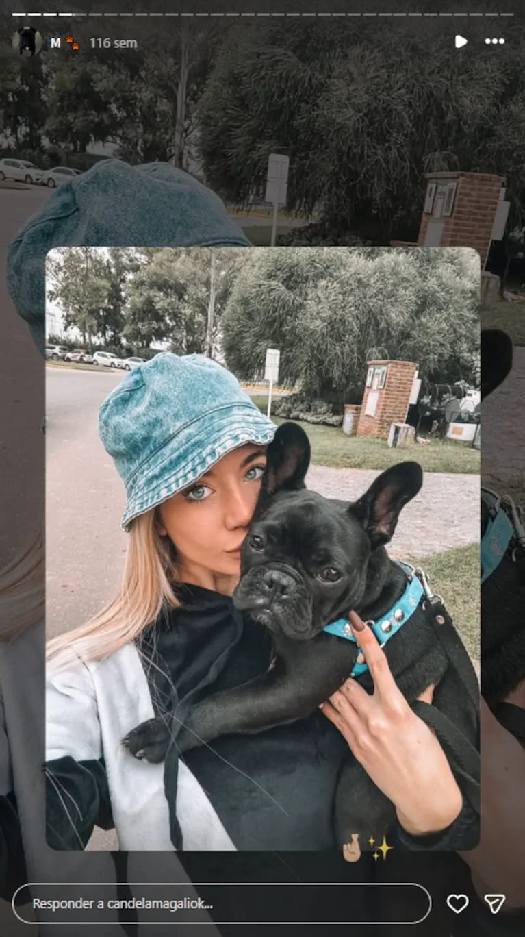 Una mujer con gorro piluso celeste sostiene a un perro bulldog francés negro a upa en la calle.