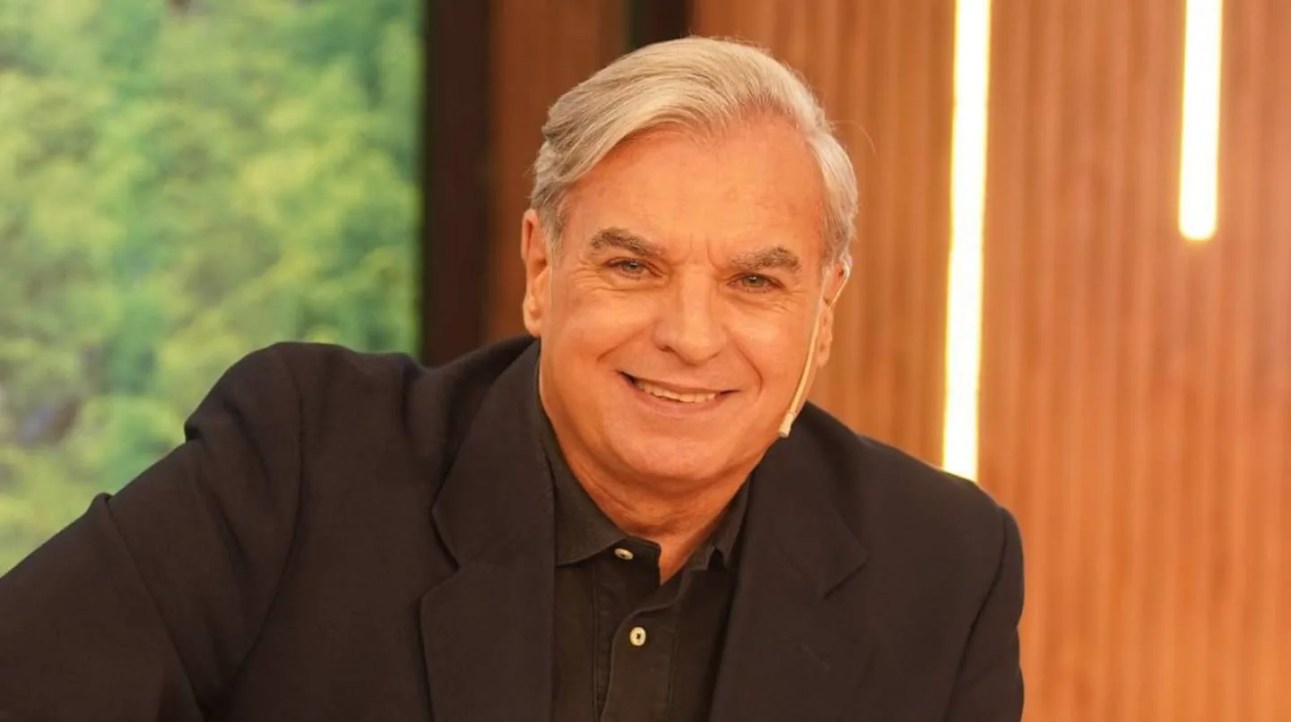 Carlos Monti sonríe vistiendo un saco oscuro y camisa negra en un estudio de televisión.