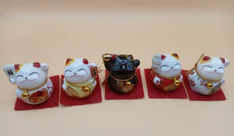 Cinco figuras pequeñas de gatos de la suerte apoyadas sobre paños rojos individuales en una superficie clara.