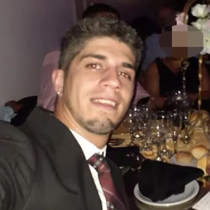Un hombre joven de traje y corbata sonrie en una mesa durante un evento social.