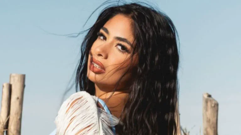 Daniela Celis mira por encima de su hombro al aire libre con el pelo suelto al viento.