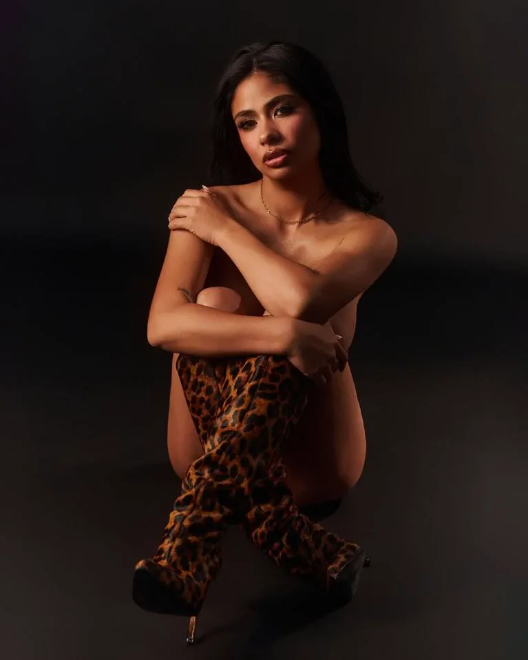 Daniela Celis posa sentada en el suelo con botas bucaneras de leopardo sobre un fondo negro.