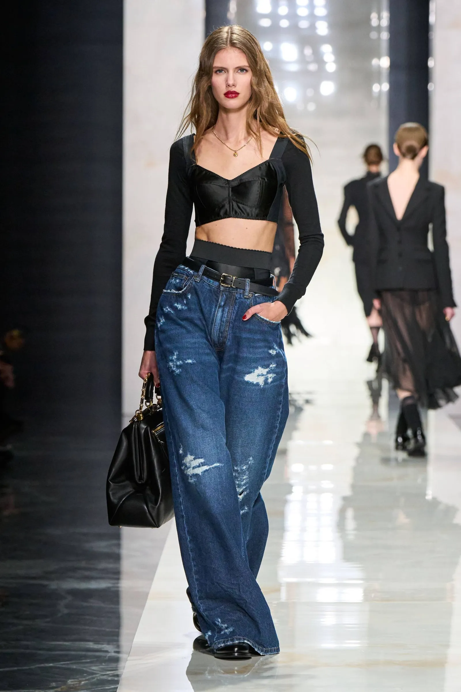 Una modelo desfila por una pasarela con un top negro y jeans anchos.