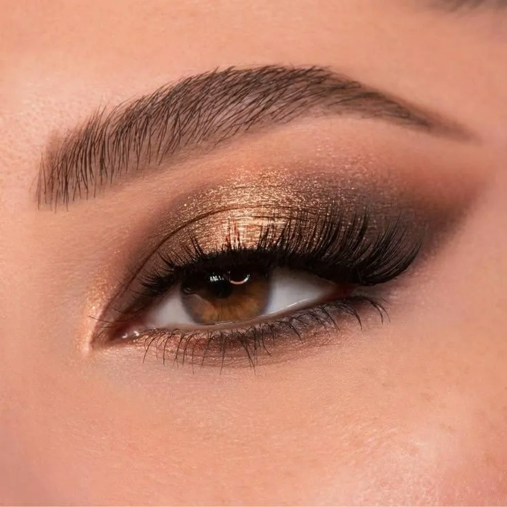 Primer plano del ojo de una persona con sombras doradas brillantes y pestañas postizas.