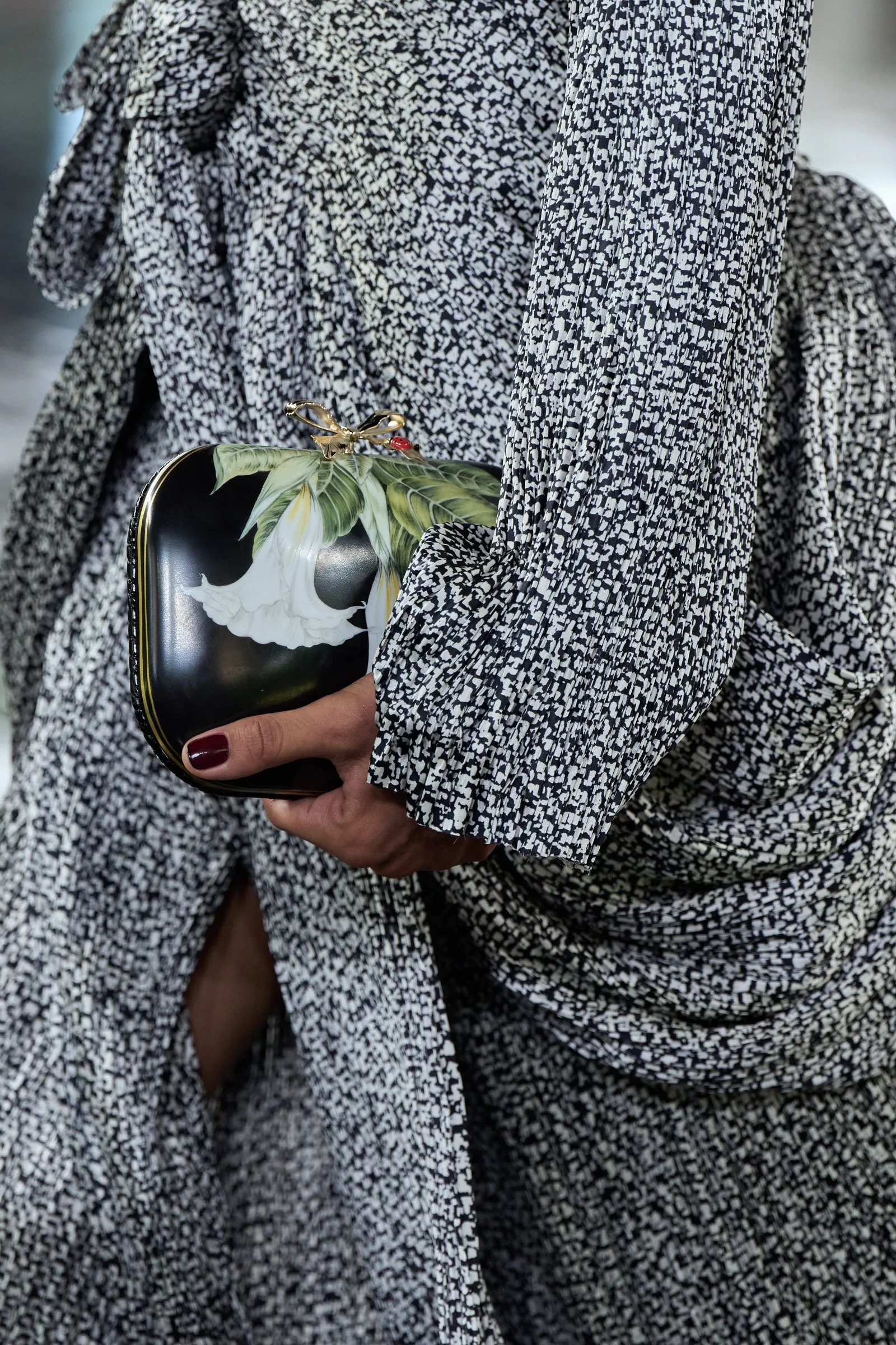 Una persona con vestido estampado en blanco y negro sostiene una cartera rígida con flores pintadas.