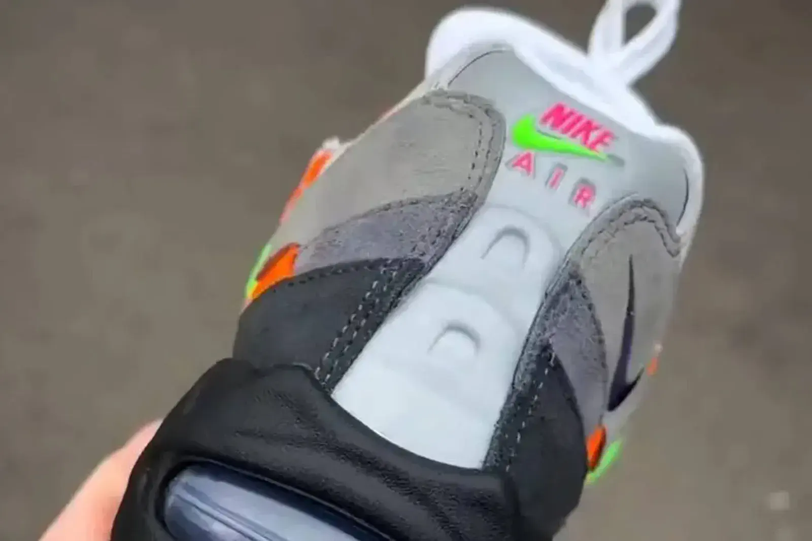 Detalle del talón de una zapatilla gris y negra con la inscripción Nike Air en letras de colores.