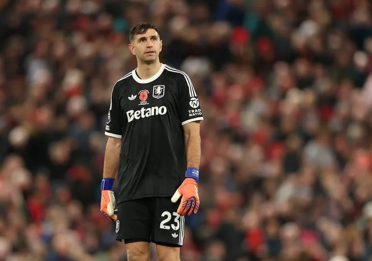 Emiliano Martinez vestido de arquero con guantes y la camiseta negra de Aston Villa parado en una cancha.
