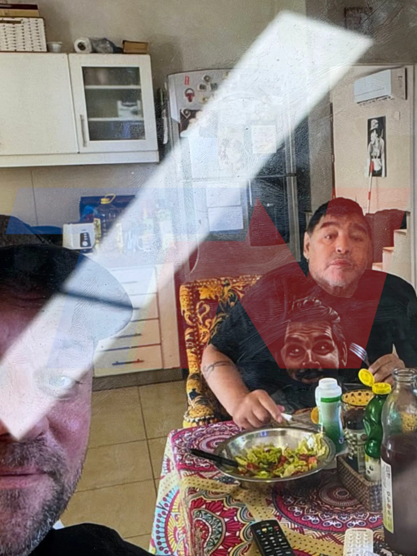 Diego Maradona sentado a la mesa frente a un bol con ensalada junto a otra persona en primer plano.