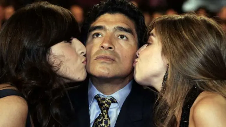 Diego Maradona con traje y corbata recibe un beso en cada mejilla de Dalma y Gianinna Maradona.