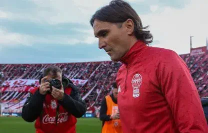 Diego Martínez camina por el césped mientras un fotógrafo le apunta con su cámara frente a la tribuna.