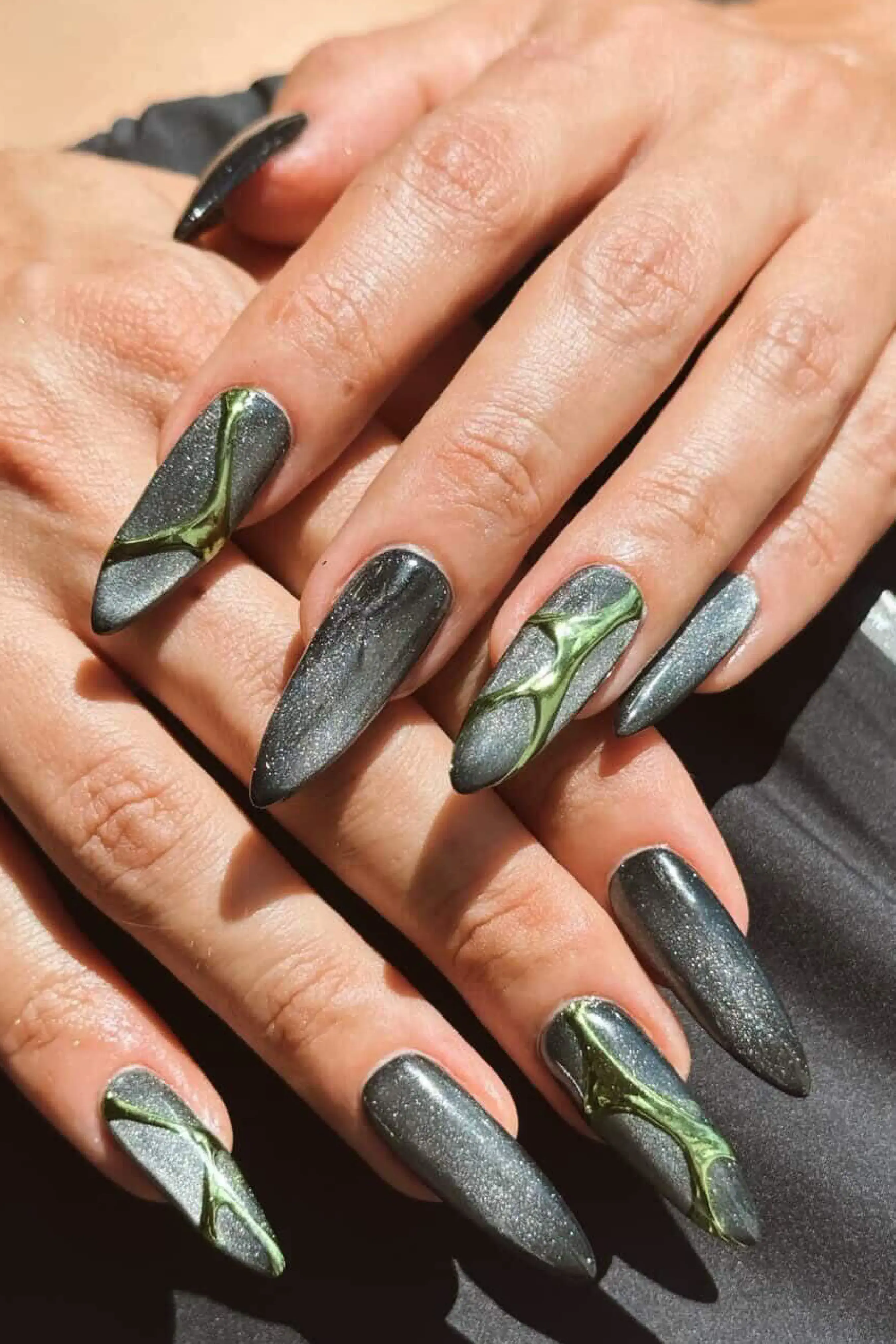 Dos manos muestran unas largas y puntiagudas con esmalte plateado y relieves verdes.