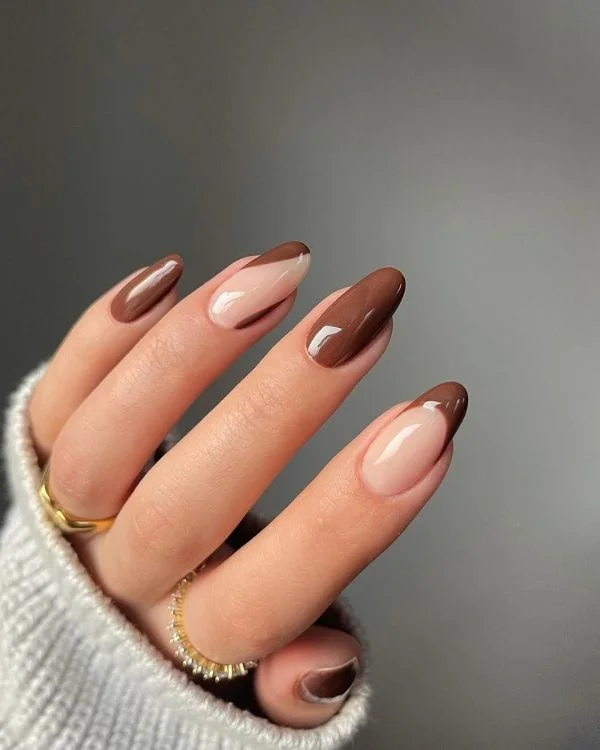 Mano con anillos dorados y unas pintadas de color marron con disenos combinados.