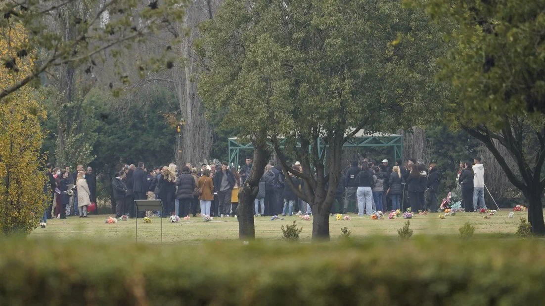 Un grupo numeroso de personas reunidas en el pasto de un parque o cementerio arbolado.