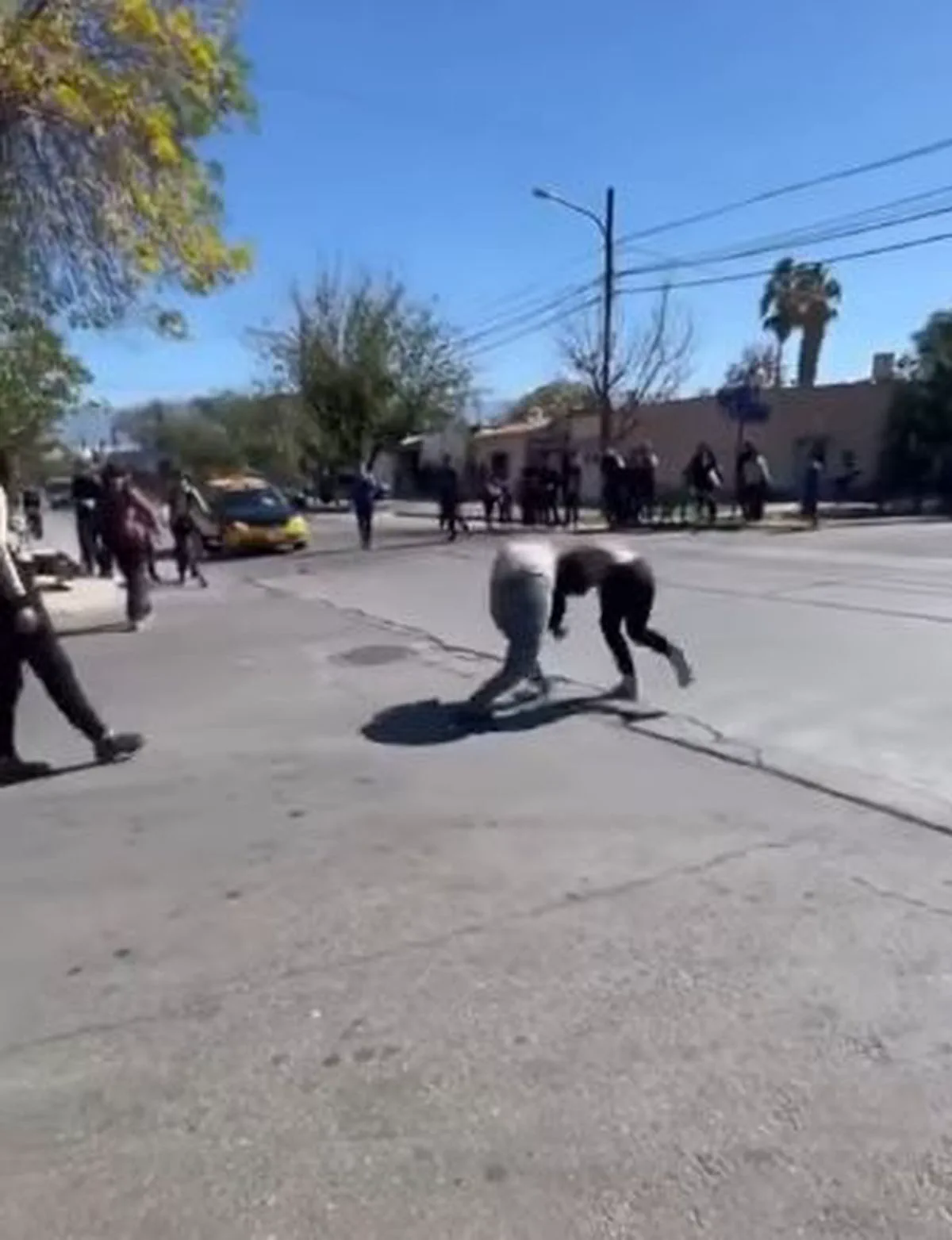 Dos personas pelean agachadas en medio de una calle mientras otros peatones observan.