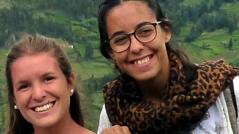 Dos mujeres sonrien a la camara al aire libre con colinas verdes detras; una de ellas lleva anteojos y bufanda animal print.