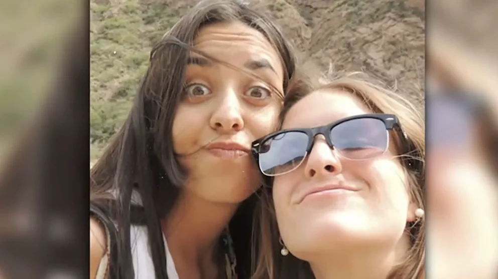 Dos mujeres sonrien en primer plano al aire libre, una haciendo muecas y la otra con anteojos de sol.