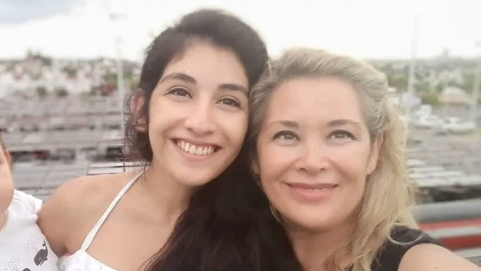 Dos mujeres sonríen abrazadas en un plano cercano al aire libre.