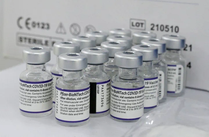 Varios frascos de vidrio con tapa metálica y etiquetas de vacunas contra el Covid-19 están agrupados sobre una superficie.
