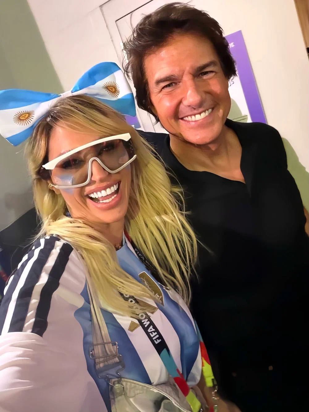 Tom Cruise sonríe junto a Vicky Xipolitakis, quien viste un moño y camiseta con los colores argentinos.
