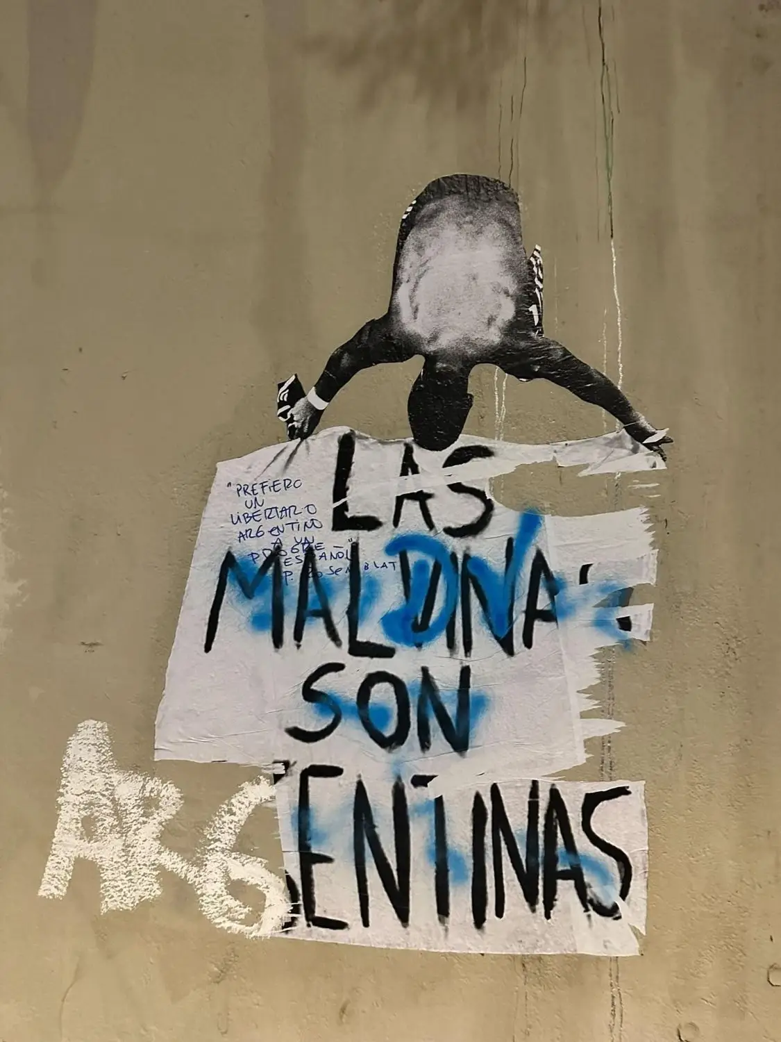 Un afiche y una pintada en una pared con la frase «Las Malvinas son argentinas» junto a una figura recortada.