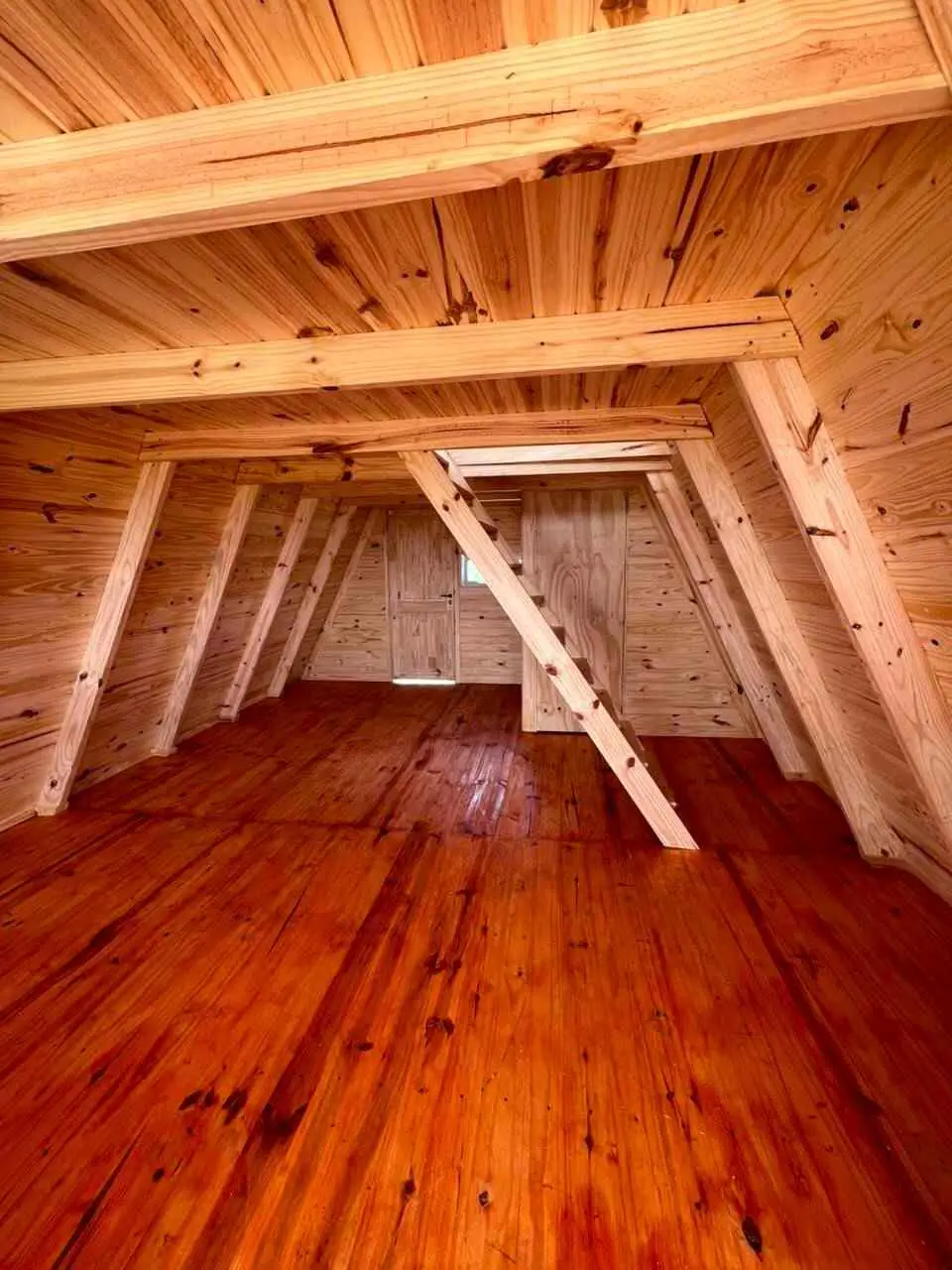 Planta alta abuhardillada de madera con vigas a la vista, piso lustrado y el hueco de la escalera.
