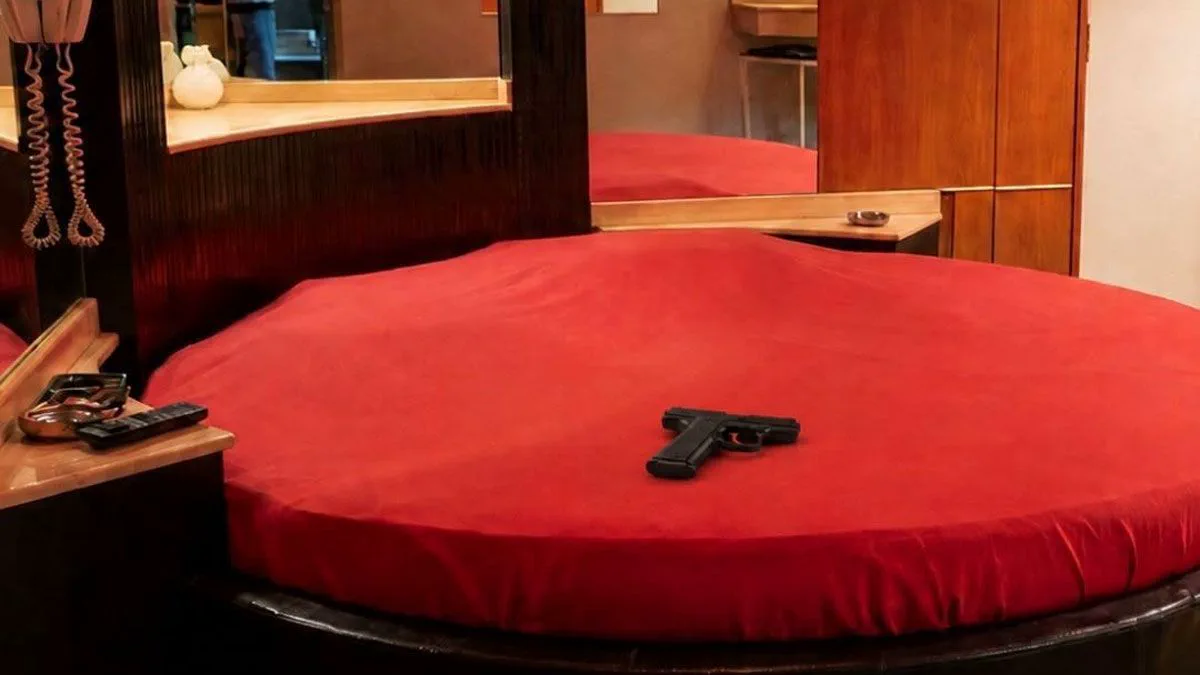 Una pistola negra reposa sobre una cama redonda cubierta con una sábana roja.