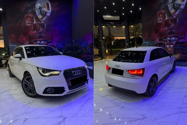 Un auto blanco Audi en un salon con iluminacion azul y cuadros de fondo.
